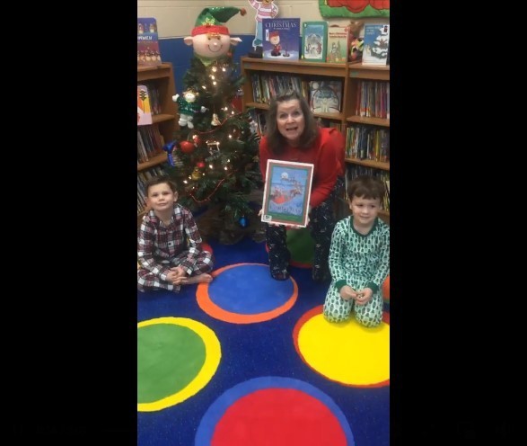library with woman and two little boys in front of a christmas tree. books on bookshelves are in the background. a christmas elf is on top of the christmas tree. there's polka-dotted carpeting.
