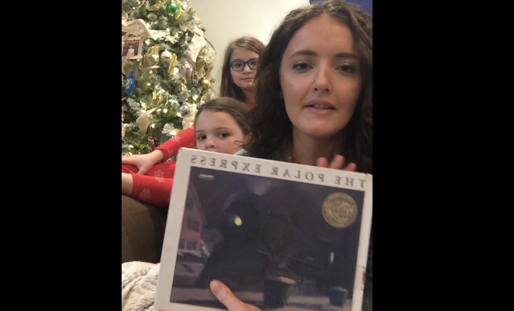 one adult and two children in front of a christmas tree holding a book called the polar express